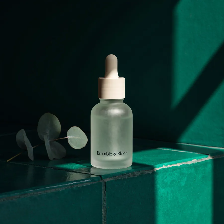 Concept product photograph: a frosted green serum bottle on emerald tile.